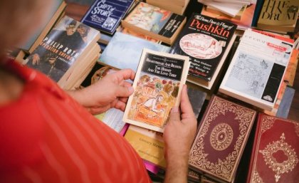 Thousands of books, magazines, and other items will be on sale at the Book Fair. Woman holding old book with other books in background at Book Fair.
